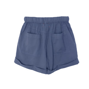 The Declan Short by Xirena is made from lightweight blue woven cotton with an elastic waistband, side seam pockets, and rolled cuffs, shown on a white background.