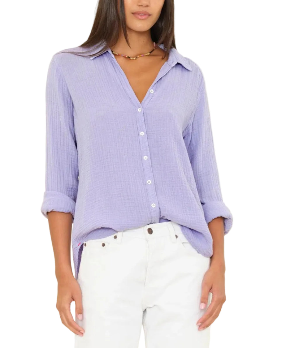A person wears the Xirena Scout Shirt in light purple crinkled cotton gauze with rolled sleeves, paired with white pants, shown from shoulders to upper thighs.