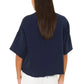 A person facing away from the camera against a white background is wearing the Xirena Romeo Sweatshirt Tee—a loose-fitting, boxy navy blue top with raw-edge sleeves—paired with white pants.