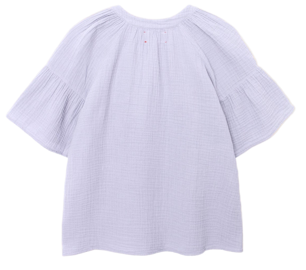 The Nia Top by Xirena is a loose-fitting, light purple cotton gauze popover with a round neckline, gathered shoulder detailing, and flutter sleeves, shown against a white background.