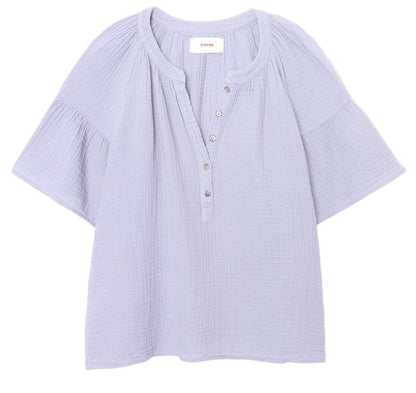 The Nia Top by Xirena is a light purple cotton gauze popover with short flutter sleeves, a round collar, button placket, and loose-fitting textured fabric.