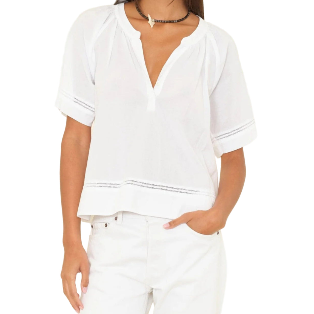 A woman wears the Xirena Sadie Top, a loose-fitting white cotton poplin short-sleeve blouse with a V-neck, styled with white pants and a black choker necklace.