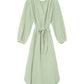 The Josephine Dress by Xirena is a light green V-neck midi with blouson sleeves, waist tie, and relaxed fit in soft cotton gauze. Knee-length style shown on a white background.