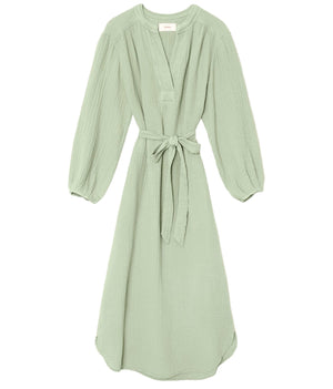The Josephine Dress by Xirena is a light green V-neck midi with blouson sleeves, waist tie, and relaxed fit in soft cotton gauze. Knee-length style shown on a white background.