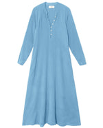 The Xirena Tabitha Dress is a light blue cotton gauze midi with long raglan sleeves, a buttoned placket, and a flowy, loose fit, shown on a white background.