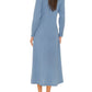 A woman is shown from the back wearing the Xirena Tabitha Dress, a flowy midi dress with long sleeves, paired with blue and brown moccasin-style shoes.