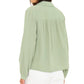 A woman is seen from the back wearing the Xirena Julianne Shirt, a light green collared, long-sleeve button-front top, paired with white pants against a plain background.