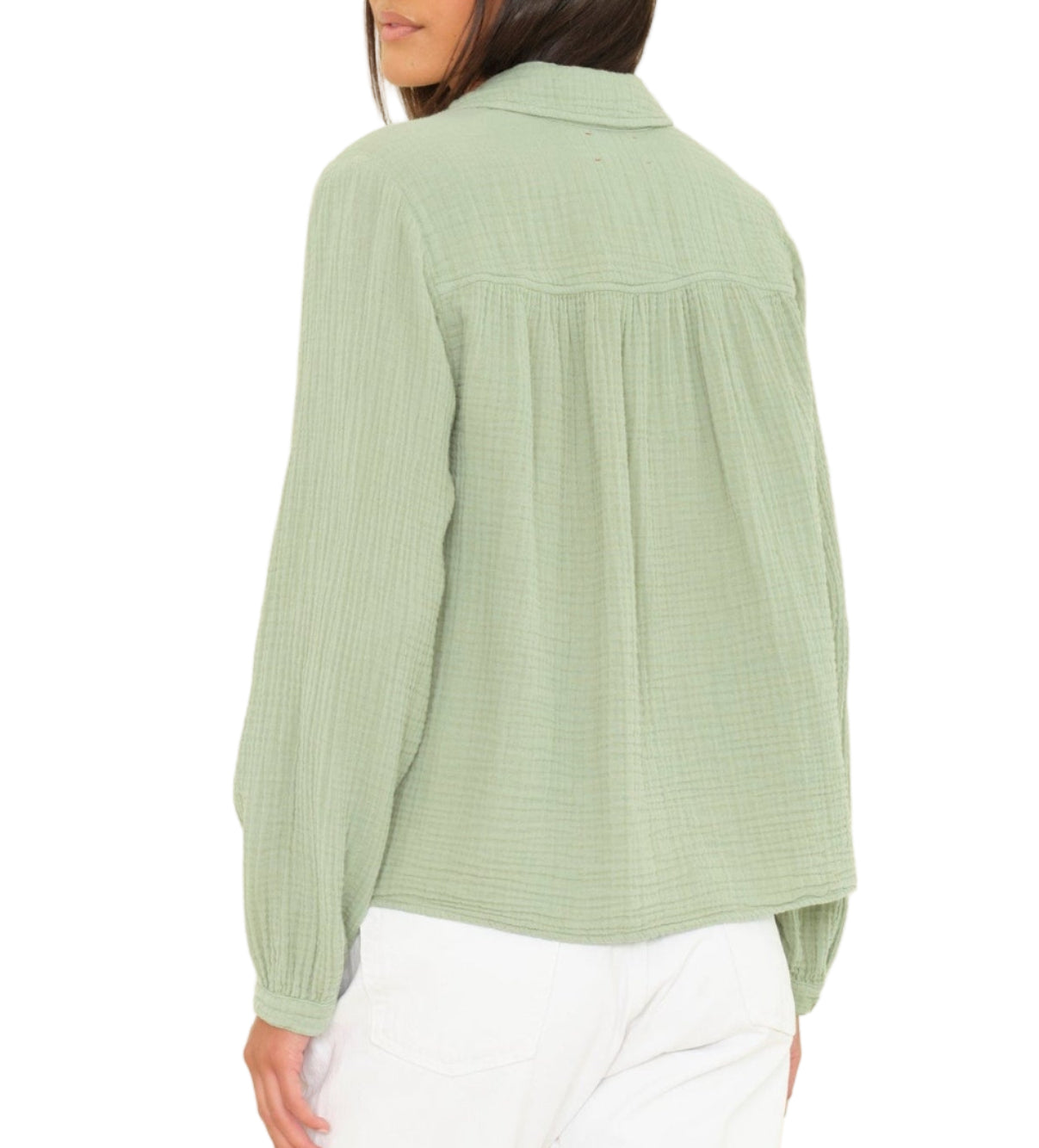 A woman is seen from the back wearing the Xirena Julianne Shirt, a light green collared, long-sleeve button-front top, paired with white pants against a plain background.