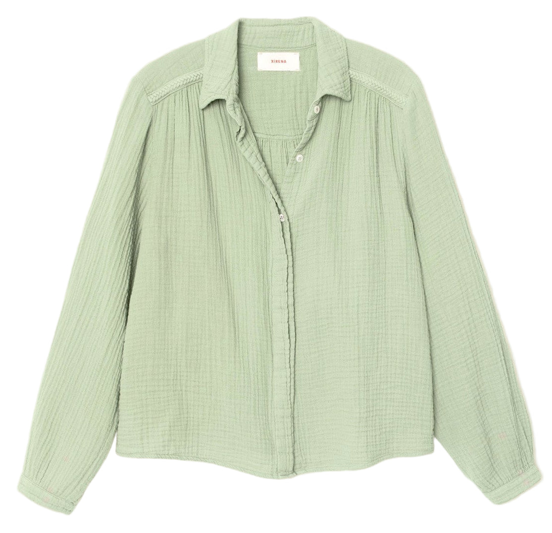 The Julianne Shirt by Xirena is a light green, long-sleeve button-front shirt with a textured fabric, collar, and subtle braided trim, shown laid flat on a white background.