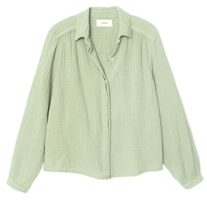 The Julianne Shirt by Xirena is a light green, long-sleeve button-front shirt with a textured fabric, collar, and subtle braided trim, shown laid flat on a white background.