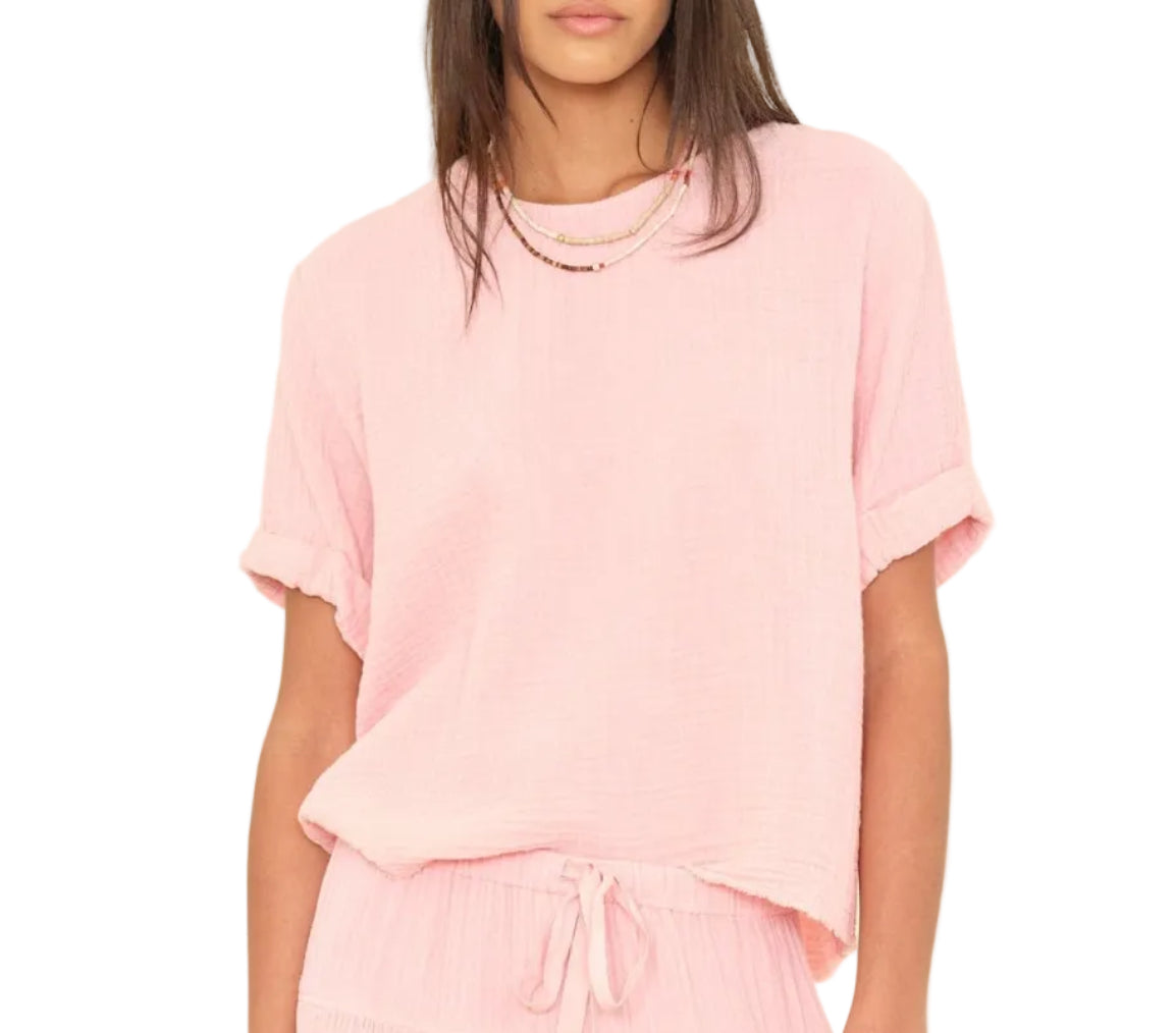 A woman wears the Xirena Carson Top—light pink, scoop neck popover style—in washed cotton gauze, paired with matching drawstring pants and layered necklaces, against a white background.