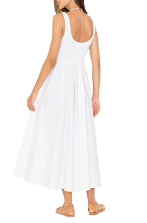 A woman, back turned against a white background, wears the Xirena Florence Dress—a sleeveless midi sundress with a smocked bodice and square neck—paired with tan sandals.