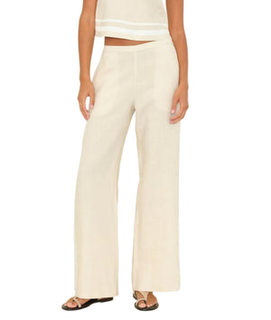 A person wearing the Xirena Pippen Linen Pant—cream-colored, wide-leg, lightweight linen with an elastic waist—paired with a sleeveless matching top and black sandals, stands against a white background.