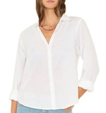 A woman wears the Xirena Bowie Shirt, a lightweight cotton poplin top with rolled cuffs and a relaxed modern silhouette, paired with light blue jeans.