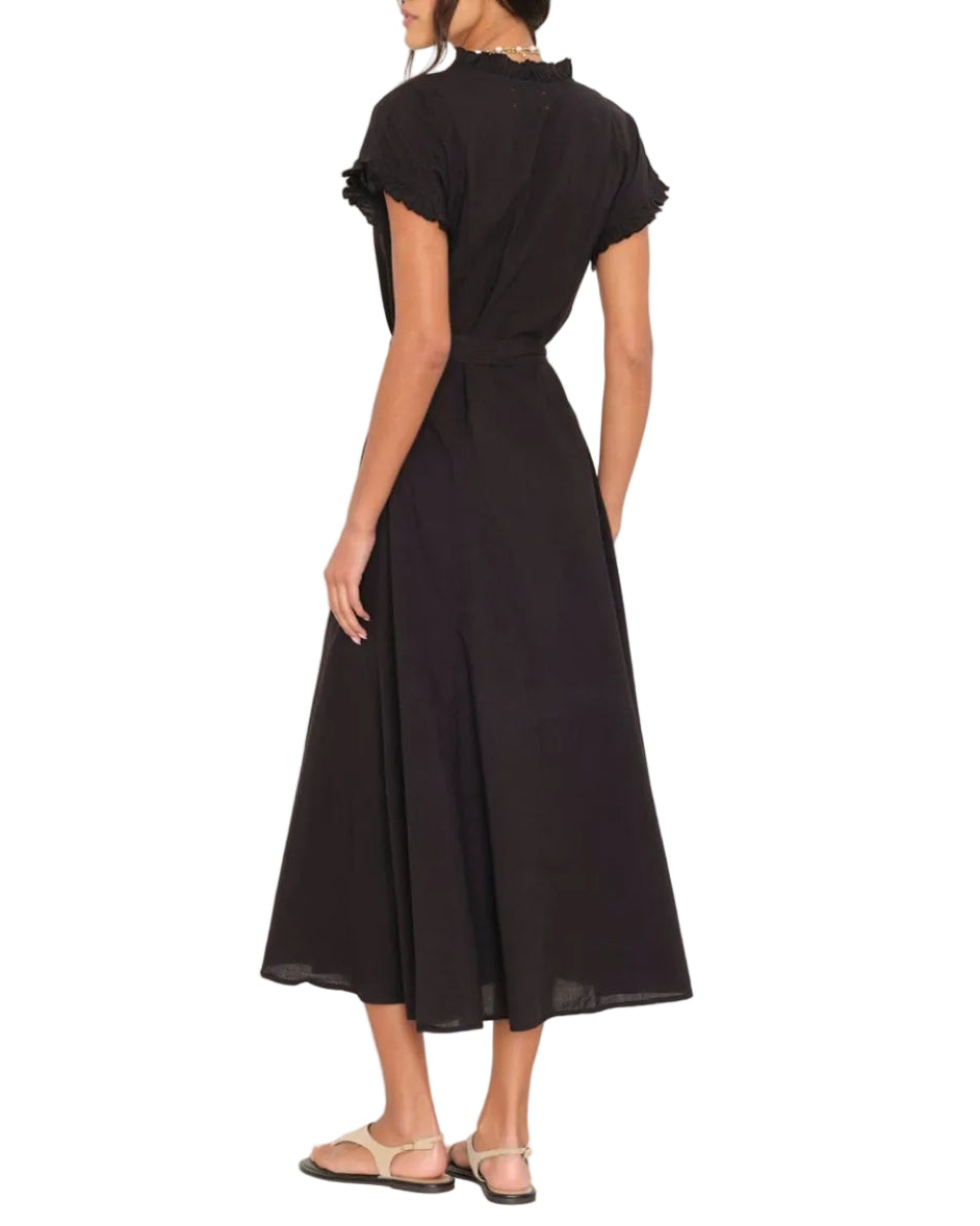 A woman seen from the back wears the Xirena Dixie Dress—a black, short-sleeve, button-front midi dress with ruffle details—paired with flat sandals.