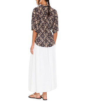 A person stands facing away, wearing a dark patterned shirt, sandals, and the Xirena Evelyn Skirt—a flowing white cotton gauze A-line pull-on skirt with an elastic waist.