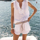A woman stands by the water with boats in the background, wearing the Xirena Portia Top— a sleeveless V-notch neck cotton gauze top paired with matching shorts and a braided belt.