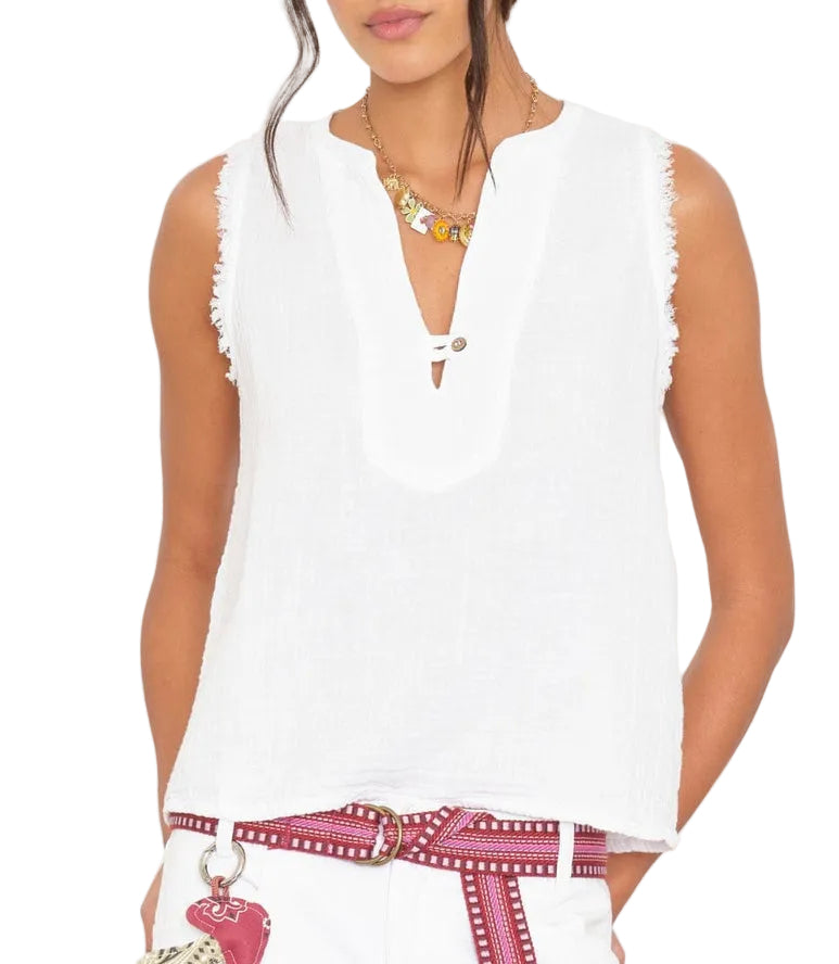 A woman wears the Xirena Portia Top—a sleeveless washed cotton gauze blouse with a V-notch neck—paired with a red patterned belt, white pants, necklace, and a visible bag.