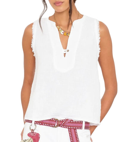 A woman wears the Xirena Portia Top—a sleeveless washed cotton gauze blouse with a V-notch neck—paired with a red patterned belt, white pants, necklace, and a visible bag.