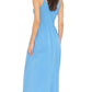 A woman stands with her back to the camera against a white background, wearing the Xirena Fallon Dress—a lightweight cotton poplin sleeveless midi dress with a full skirt—paired with brown sandals.