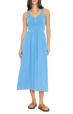 A woman stands against a white background wearing the Fallon Dress by Xirena, a lightweight cotton poplin sleeveless midi dress with front buttons, paired with brown sandals and a red necklace.