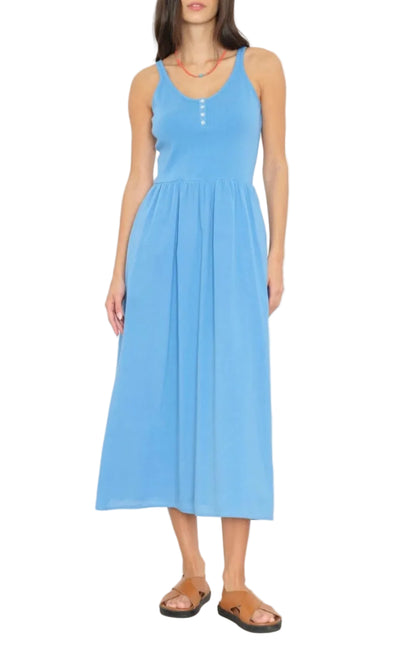 A woman stands against a white background wearing the Fallon Dress by Xirena, a lightweight cotton poplin sleeveless midi dress with front buttons, paired with brown sandals and a red necklace.