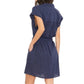 A woman is shown from the back with hands in pockets, wearing the Eliza Dress by Xirena—a navy blue cotton poplin mini shirt dress with cap sleeves—against a white background.