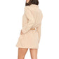 A woman wearing the Xirena Bobby Cotton Gauze Dress in beige with a brown belt, standing sideways with one hand in her pocket.