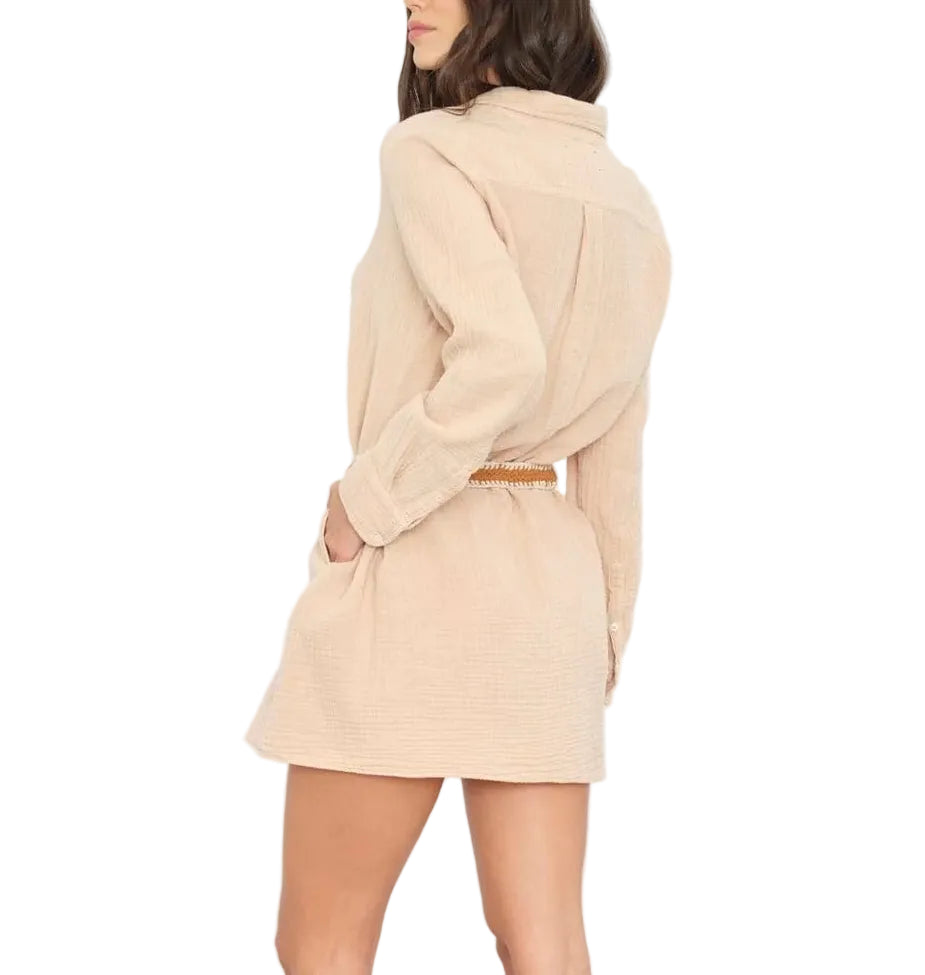A woman wearing the Xirena Bobby Cotton Gauze Dress in beige with a brown belt, standing sideways with one hand in her pocket.