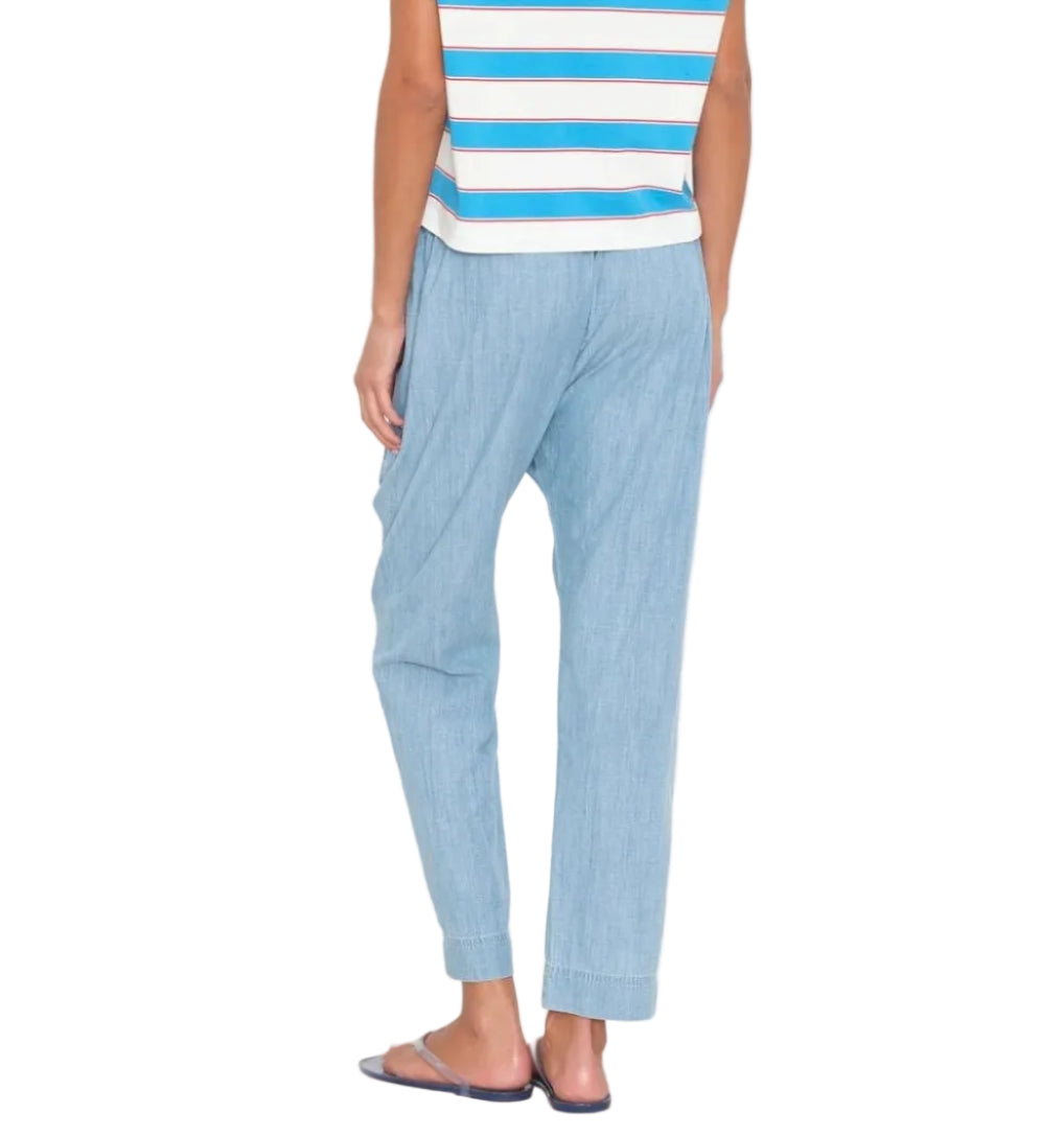 Person standing with back to the camera, wearing a sleeveless striped top, Xirena Draper Chambray Pant with a drawstring waist, and flat sandals.