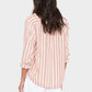 A person with long brown hair wears a pink and white Bowie Stripe Shirt by Xirena, a striped viscose-linen button-up with rolled sleeves and a modern silhouette, shown from the back against a plain light background.