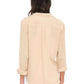 A person is seen from the back wearing the Xirena Scout Cotton Gauze Shirt in light beige with rolled sleeves, paired with white pants, set against a plain background.