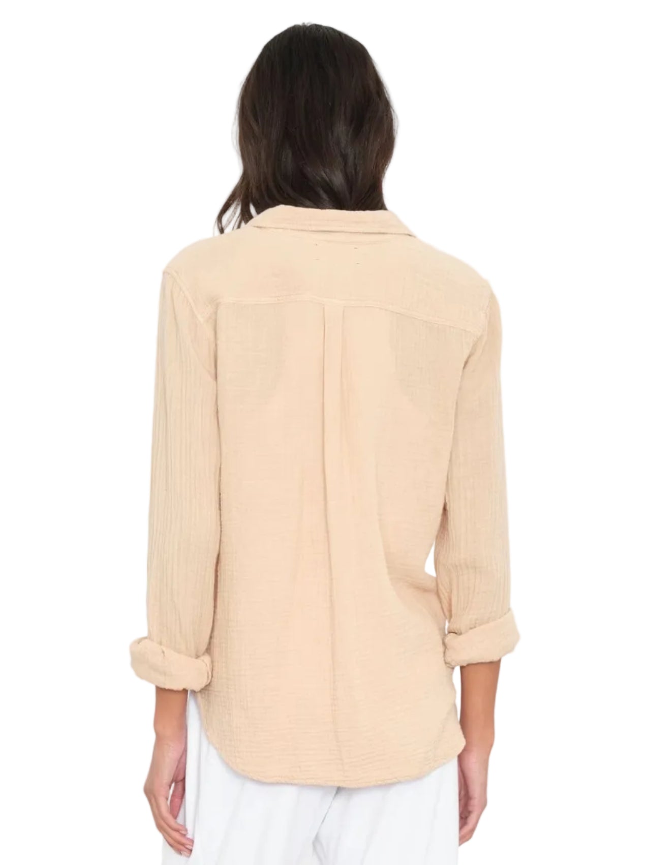 A person is seen from the back wearing the Xirena Scout Cotton Gauze Shirt in light beige with rolled sleeves, paired with white pants, set against a plain background.