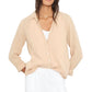 A woman wears the Xirena Scout Cotton Gauze Shirt in beige over a white top and white drawstring pants, hands in her pockets.