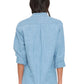 A person stands with their back to the camera wearing the Xirena Beau Chambray Shirt in light blue, styled with rolled-up sleeves and paired with white pants.