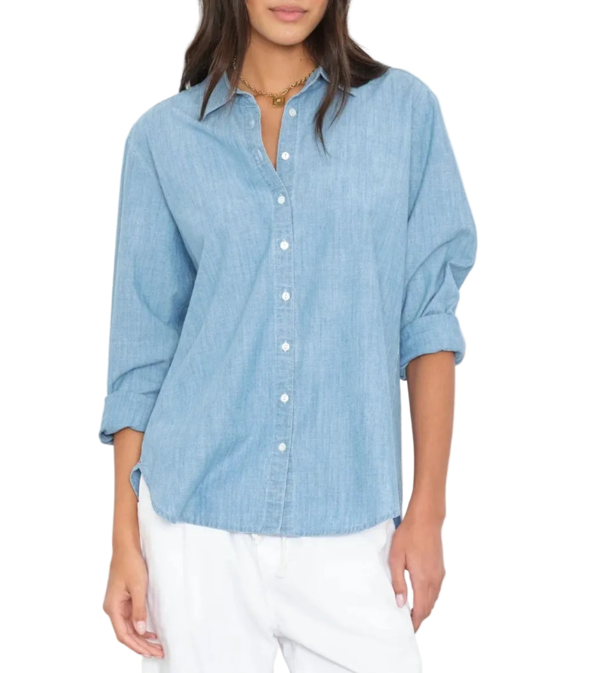 A woman wears the Xirena Beau Chambray Shirt in light blue cotton with rolled sleeves, paired with white pants for a fresh, menswear-inspired look.
