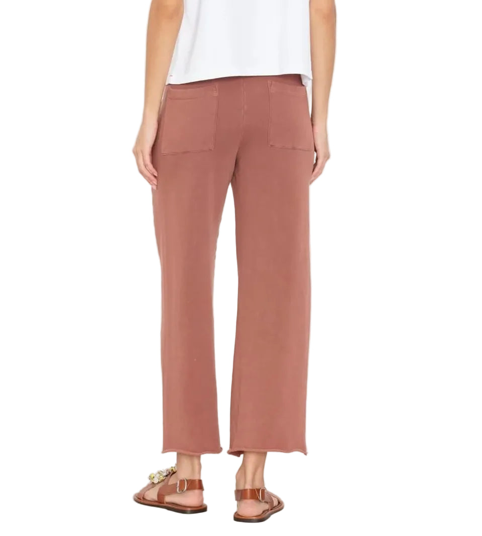 A person shown from the back wears a white top, Xirena Matteo Sweatpant—vintage washed French terry, wide-leg, rose-colored cropped ankle-length sweatpants with back pockets—and brown sandals.