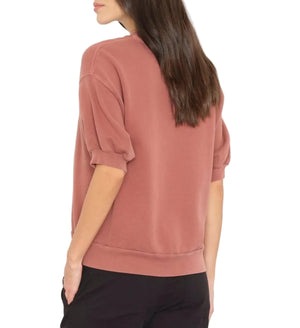 A woman wearing the Xirena Jax Sweatshirt, a vintage washed French terry short-sleeve top, and black pants stands with her back to the camera against a white background.