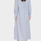 A woman stands with her back to the camera, wearing the Boden Dress by Xirena—a long-sleeved, blue and white vertical striped tailored shirtdress—paired with brown loafers.