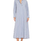 A woman wearing the Xirena Boden Dress—a long, blue-and-white vertically striped tailored shirtdress with long sleeves—and brown shoes, standing against a white background.