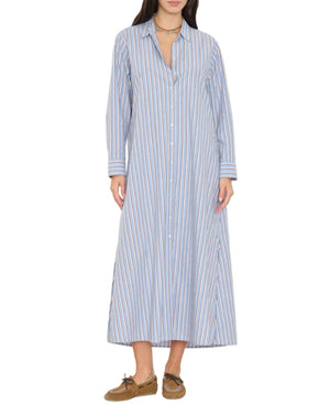 A woman wearing the Xirena Boden Dress—a long, blue-and-white vertically striped tailored shirtdress with long sleeves—and brown shoes, standing against a white background.