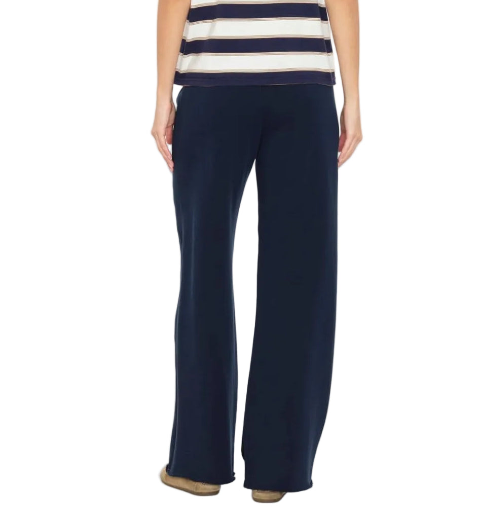A person wearing the Xirena Renzo Sweatpant in navy blue, featuring a wide-leg silhouette and an elasticized drawstring waist, paired with a short-sleeved striped top; photographed from the back against a white background.