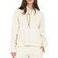 A woman wearing the Xirena Chase Sweatshirt, a relaxed hoodie made from ultra-soft fleece with a kangaroo pocket and beige drawstrings, paired with matching off-white pants.