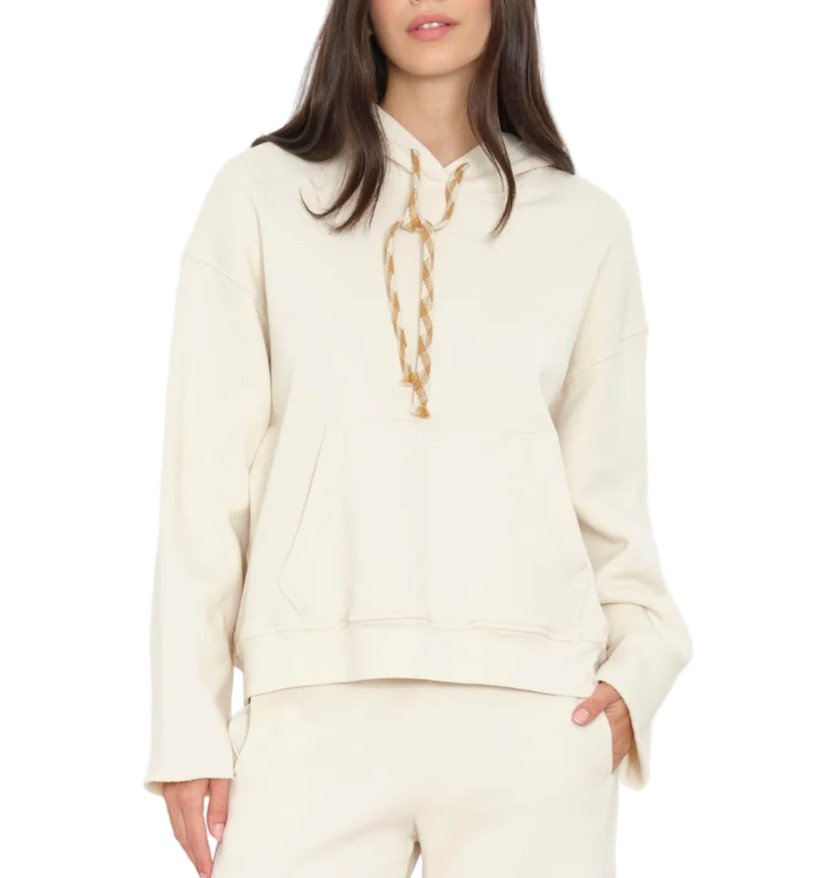 A woman wearing the Xirena Chase Sweatshirt, a relaxed hoodie made from ultra-soft fleece with a kangaroo pocket and beige drawstrings, paired with matching off-white pants.