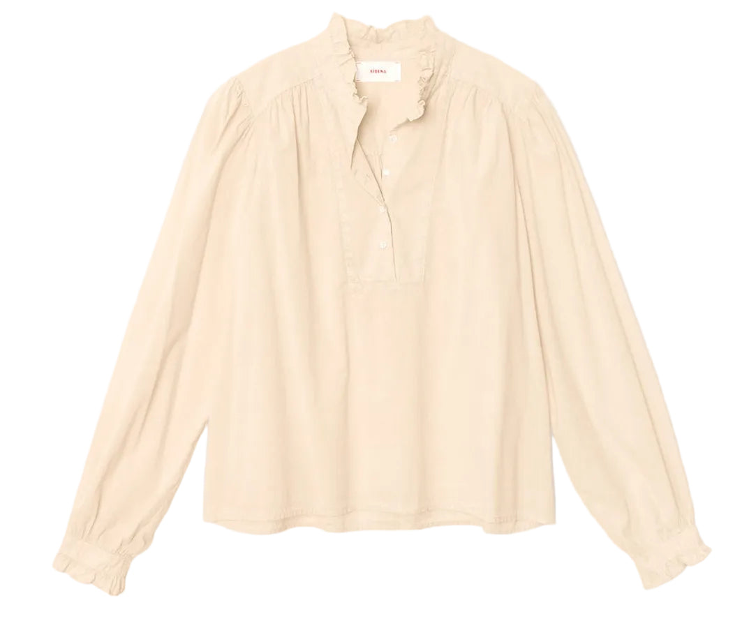 The Dorien Top by Xirena is a cream-colored, long-sleeve blouse crafted from lightweight cotton poplin, featuring a delicate ruffled collar, partial button front, and gathered blouson sleeves. It is displayed on a plain white background.