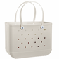 The Original Bogg Bag by Bogg Bags is a beige rectangular tote featuring two handles and small circular holes on the sides, with “bogg” embossed on the lower right corner. Stylish and practical, this washable bag is perfect for use as a beach bag or an everyday carryall.