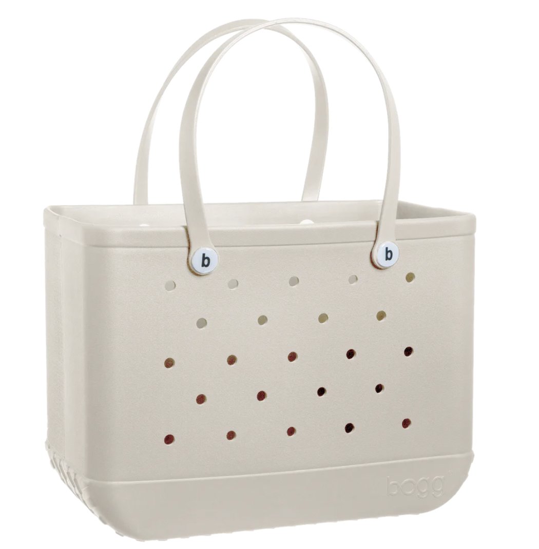 The Original Bogg Bag by Bogg Bags is a beige rectangular tote featuring two handles and small circular holes on the sides, with “bogg” embossed on the lower right corner. Stylish and practical, this washable bag is perfect for use as a beach bag or an everyday carryall.