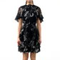 A woman wears the Jason Wu Collection SS Printed Chiffon Dress, a short black floral dress with sheer short sleeves and ruffle details, standing against a plain white background.