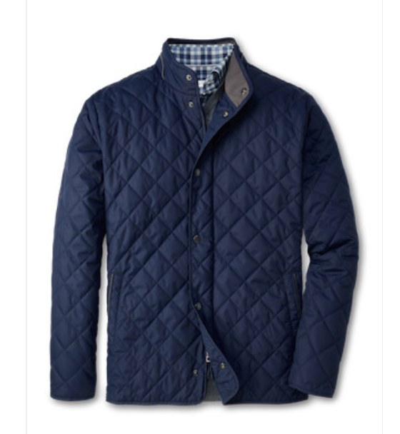 The Peter Millar Suffolk Coat, a navy blue water-resistant quilted jacket with a stand-up collar and snap buttons, is styled over a blue and white checkered shirt.