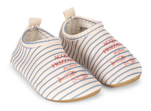 The Konges Slojd Baby and Kids’ Aster Swim Shoes are slip-on shoes for children, crafted from quick-drying fabric and designed with blue stripes, playful fish graphics, and red text on top. They feature a non-slip sole for safety and are shown against a white background.